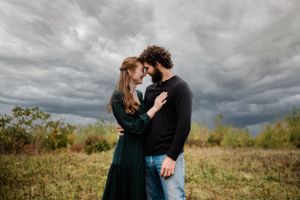 A couple embraces in a field beneath dramatic storm clouds.