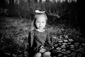 A black and white portrait of a child with a bow in their hair making a playful expression.