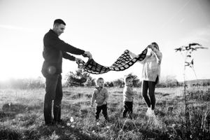 A family plays with a blanket together in a misty black and white field scene.