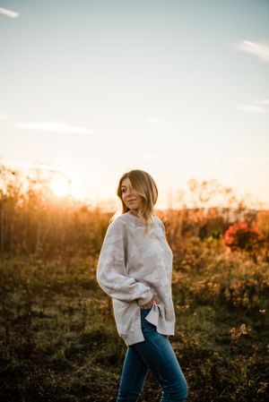 Person in white sweater and jeans dancing joyfully in a sunlit field at sunset.