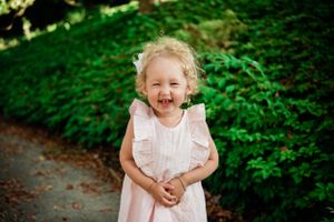 Child in white dress playing in lush green garden setting.