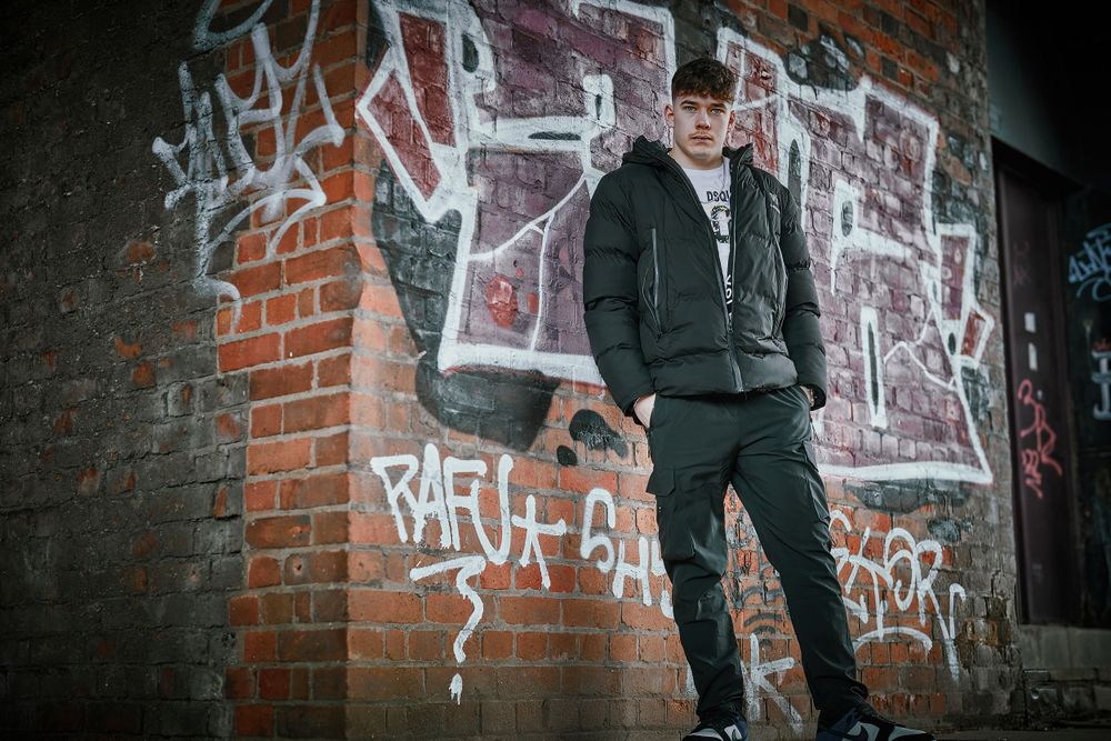 Urban photoshoot against brick wall with graffiti in moody lighting.