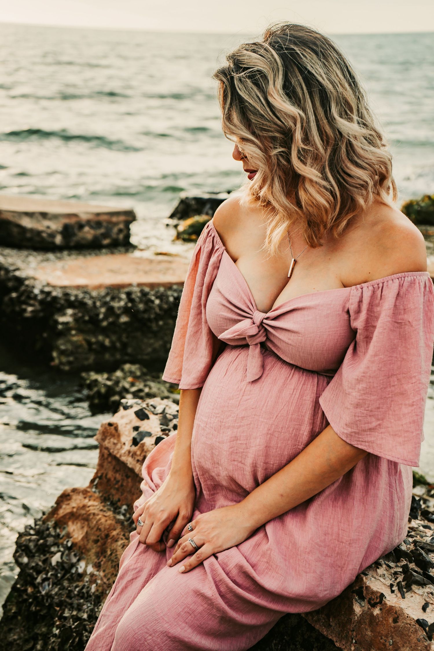 Outdoor Maternity Session at Ft. Desoto in St. Pete, FL; woman sitting on rock by the ocean