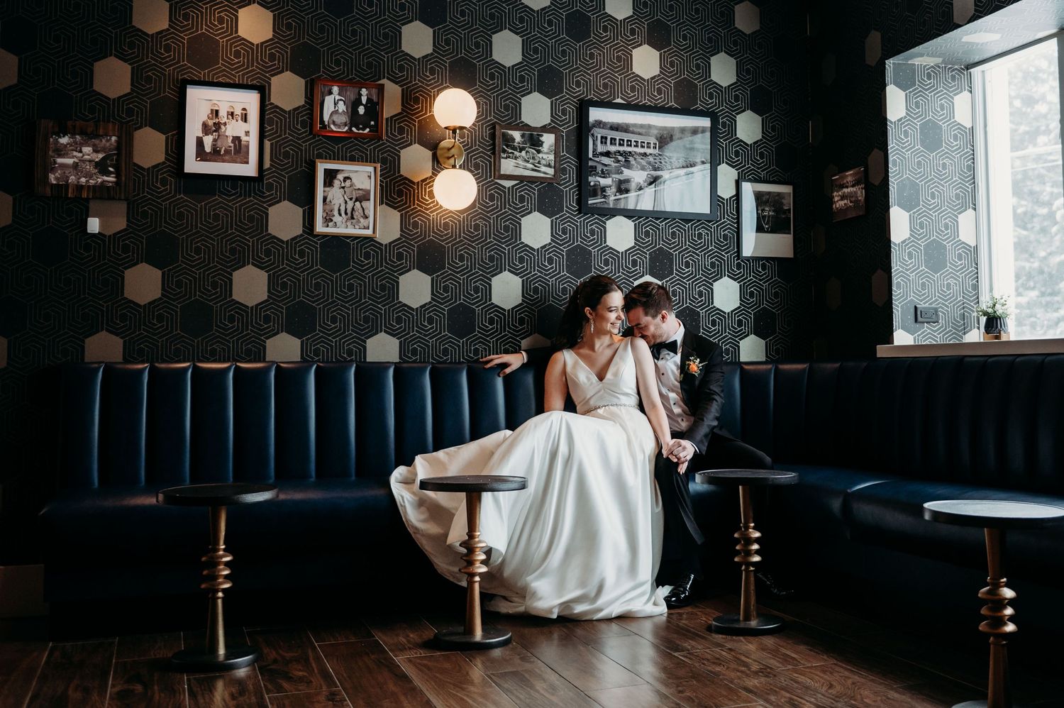 Two people in formal attire share an intimate moment on a navy blue banquette in a vintage-style bar with polka dot walls at Perona Farms.