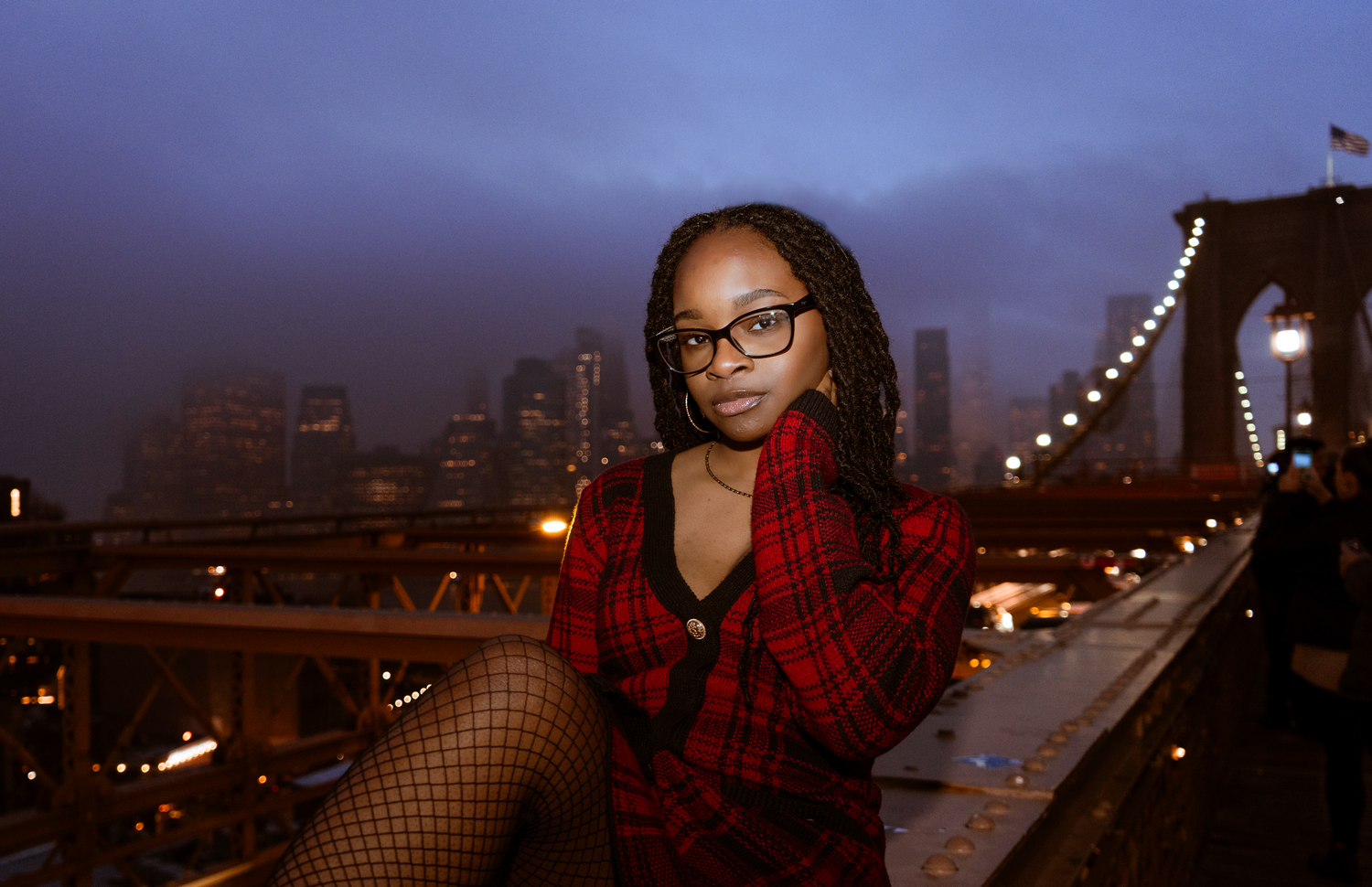 Young woman in New York City at night sitting on Brooklyn bridge