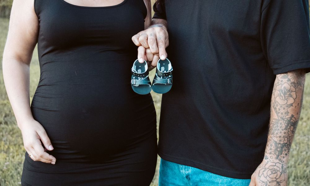 Maternity photo showing couple holding tiny teal baby shoes against black outfits.