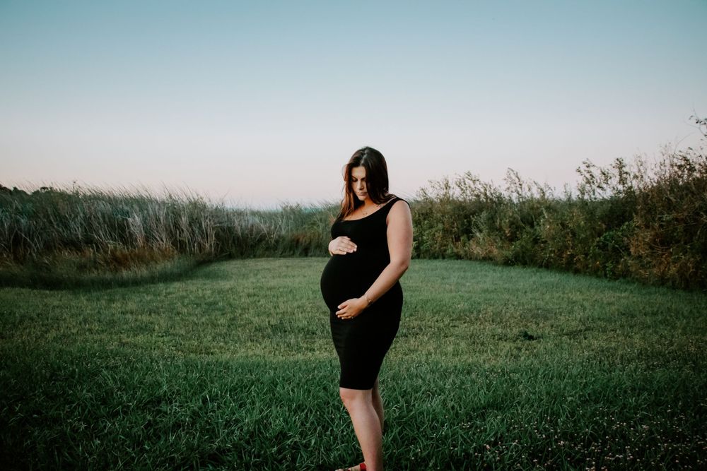 Silhouette of pregnant woman in black dress standing in field during golden hour.