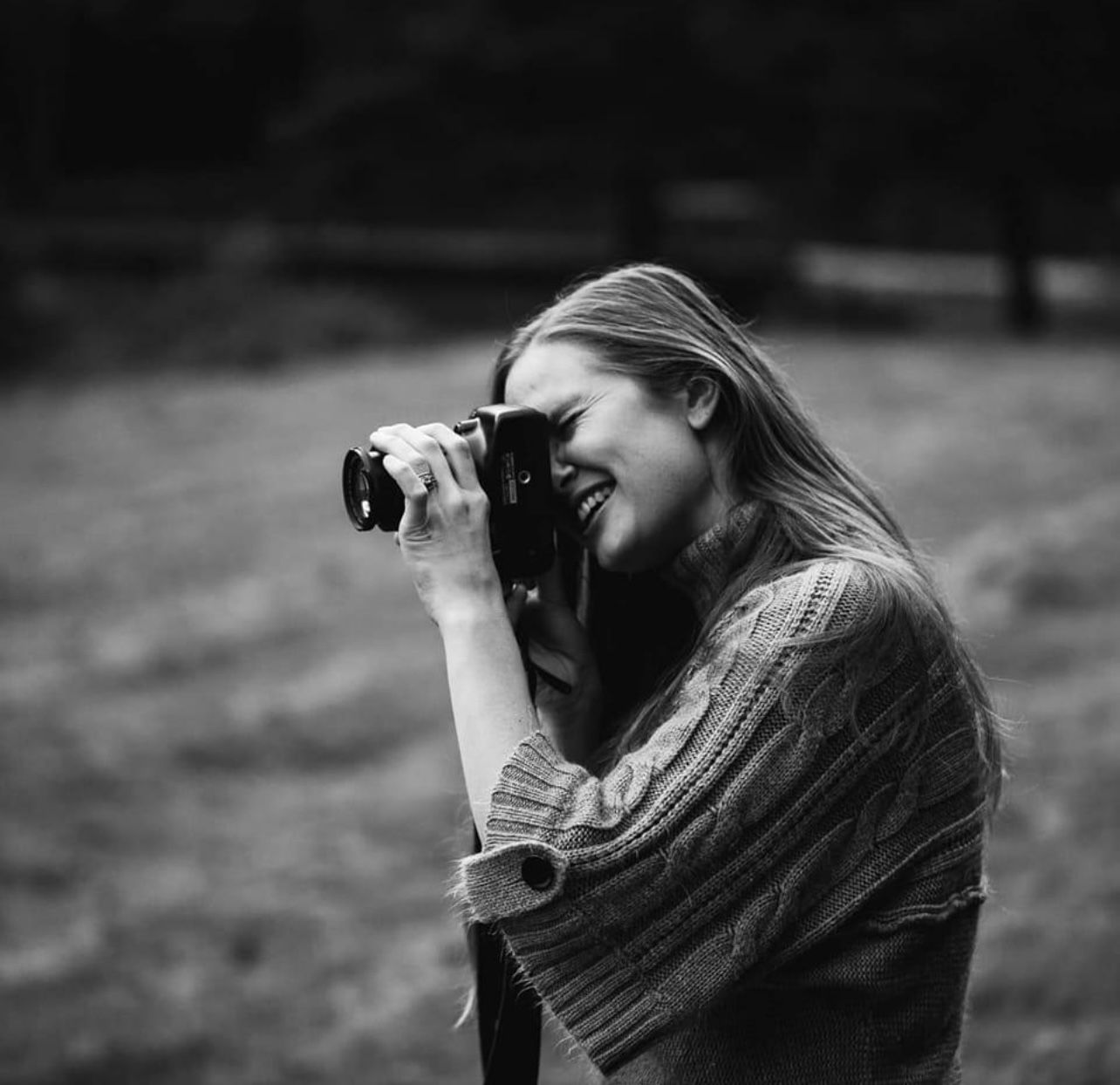 Black and white portrait of a photographer taking pictures outdoors in a knit sweater.