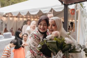 Wedding guests share a happy moment while holding flowers at an outdoor tented reception.
