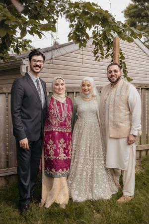 Group photo of wedding guests in traditional and modern formal attire standing in a backyard.