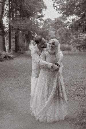 A bride and groom in matching white outfits share a playful moment in a wooded park.