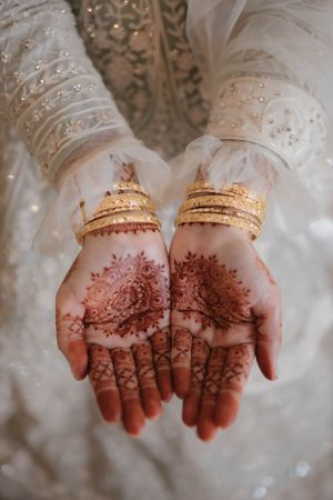 Detailed henna designs and gold bangles adorn a bride's palms during a traditional wedding ceremony.