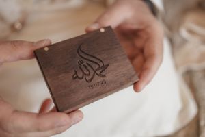 Close-up of hands holding a wooden box with Arabic calligraphy engraving.