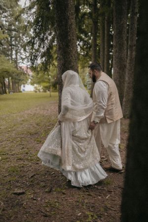Couple in traditional wedding attire walking through a pine forest.