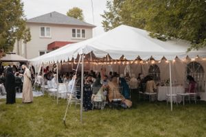 An outdoor wedding reception under white tents with guests seated at decorated tables.