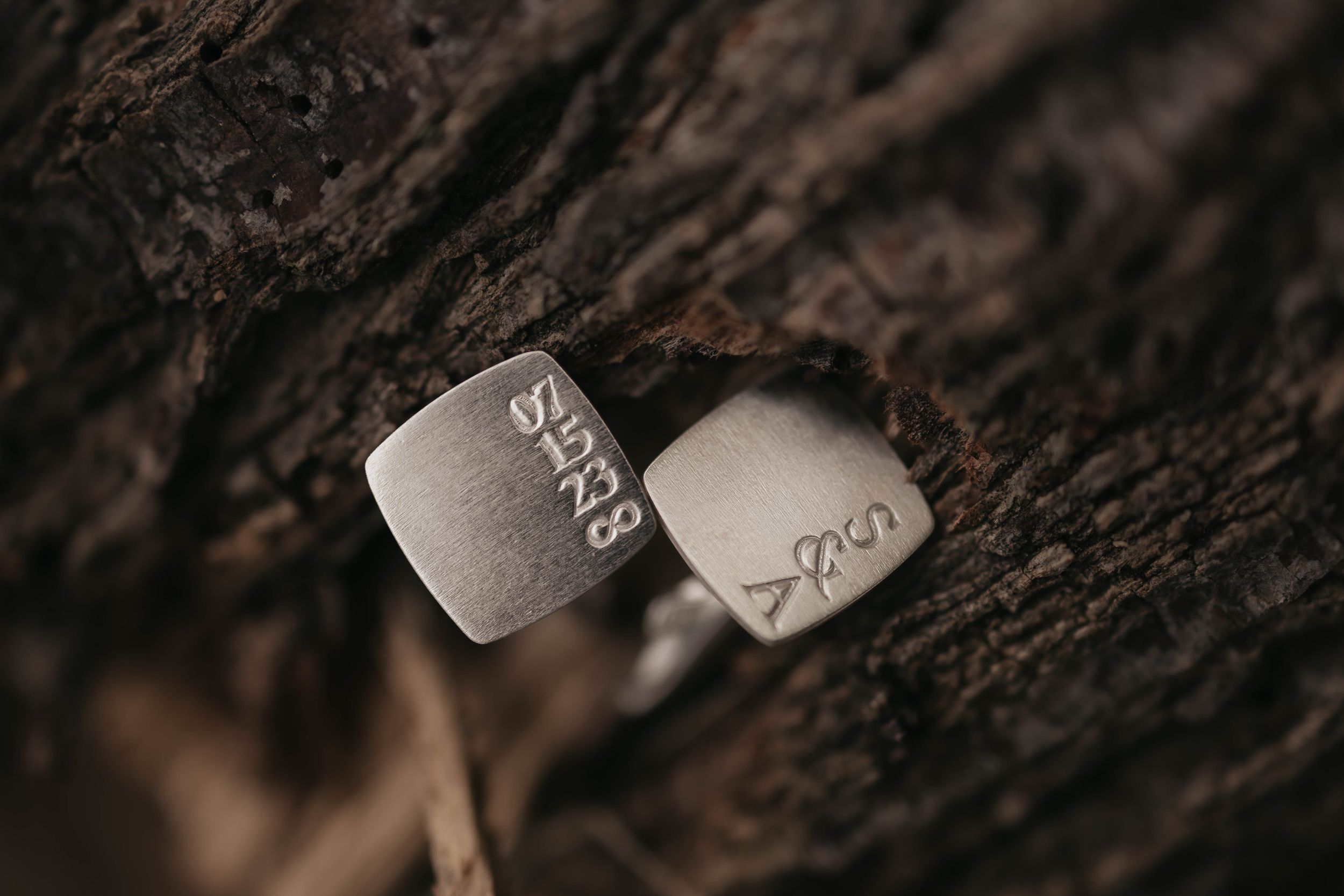 Two silver wedding rings photographed on dark textured bark.