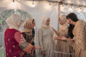 Wedding guests in hijabs and formal attire socialize under string lights at an outdoor reception.