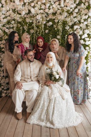 Wedding party poses together under a floral arch decorated with white roses.