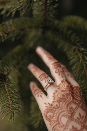 Intricate henna design on hand with engagement ring showcased against pine needles.