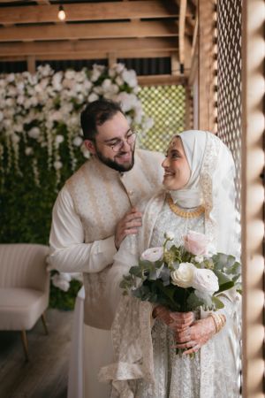 A couple sharing a tender moment against a floral wall backdrop at their wedding celebration.
