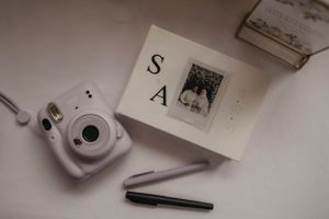 White Instax camera and stationery items arranged on a clean white surface.