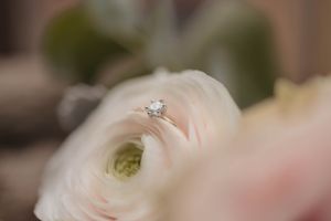 Close-up of a diamond engagement ring nestled in a white ranunculus flower.