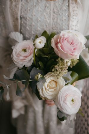 Delicate pink and white roses with greenery form an elegant bridal bouquet against lace fabric.