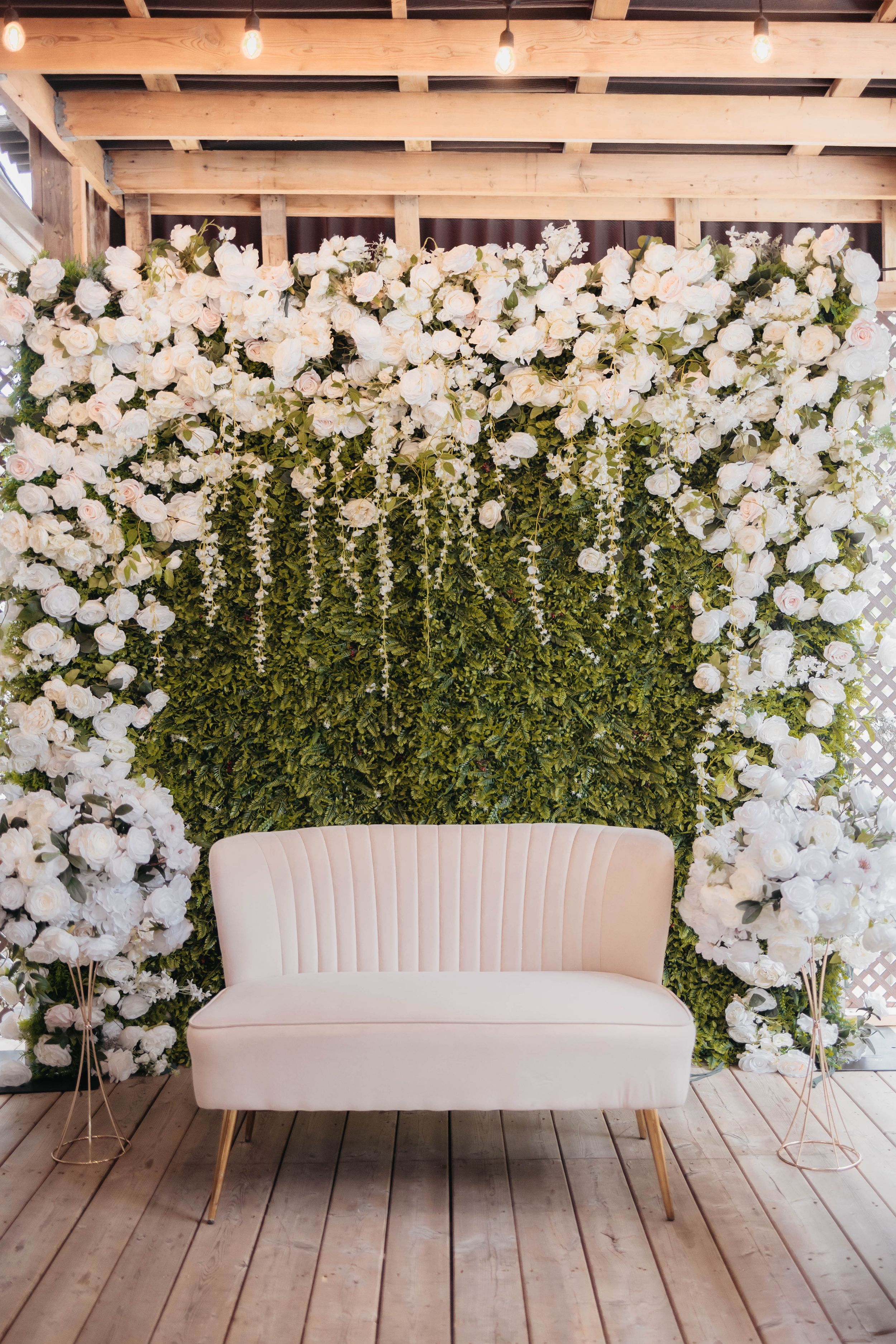Luxurious white floral wall backdrop with cream sofa and greenery for wedding photos.