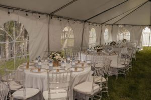 White wedding reception tent setup with round tables and elegant place settings.