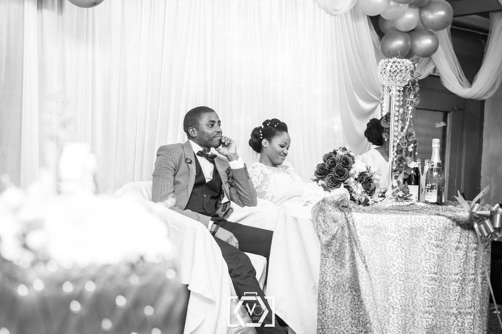 Black and white photo of a smiling bride and groom seated at their wedding reception table.