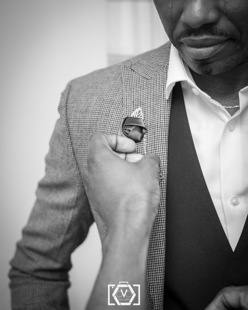 Black and white close-up of a groom in a houndstooth blazer adjusting his boutonniere.
