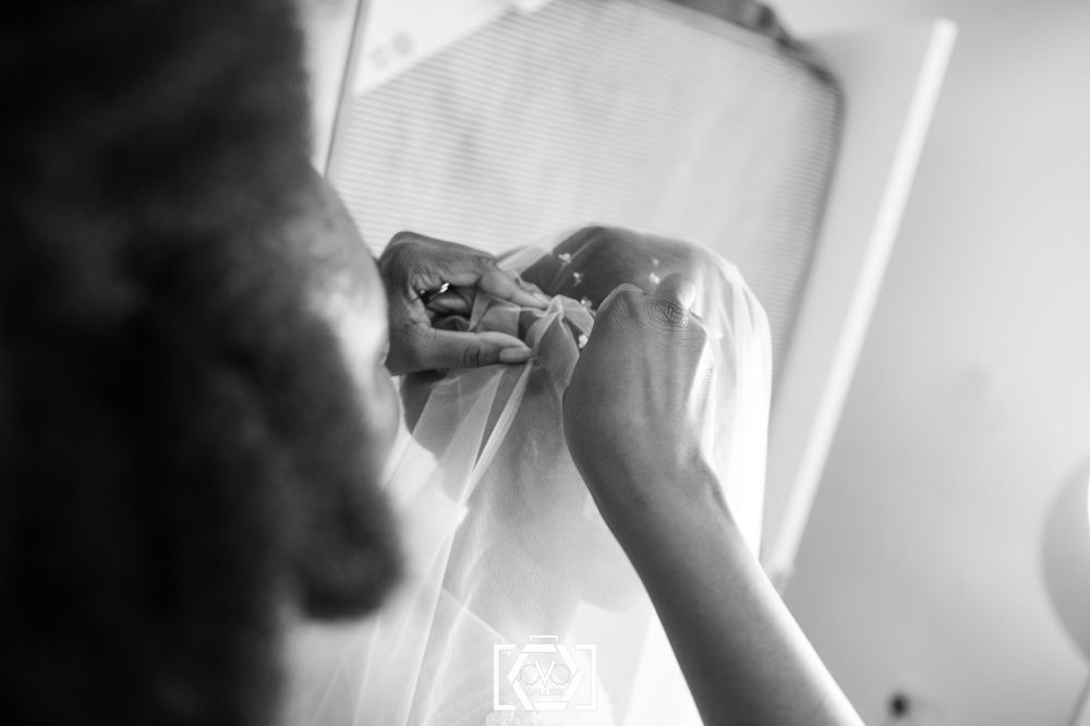 Black and white photo of hands fastening buttons on a white wedding dress bridal preparation.