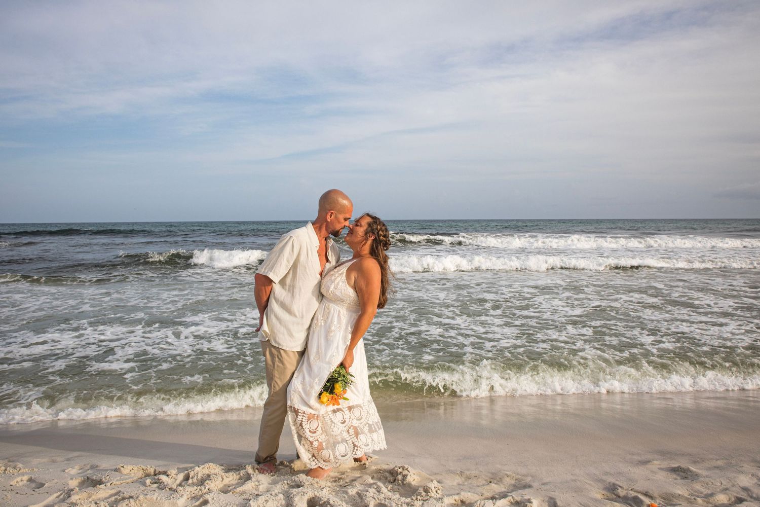 Beach wedding couple embracing by the ocean waves with sunflowers.