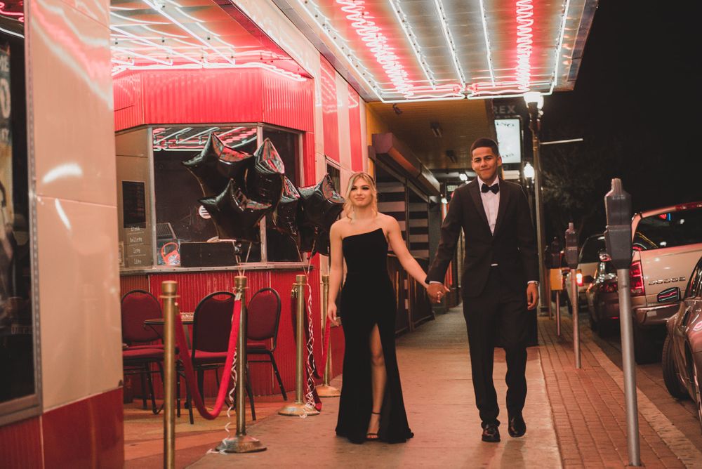 Couple walks together in formal attire under red neon lighting at night.