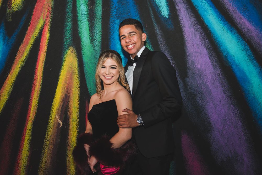 A couple in formal attire poses in front of a colorful streaked light background.