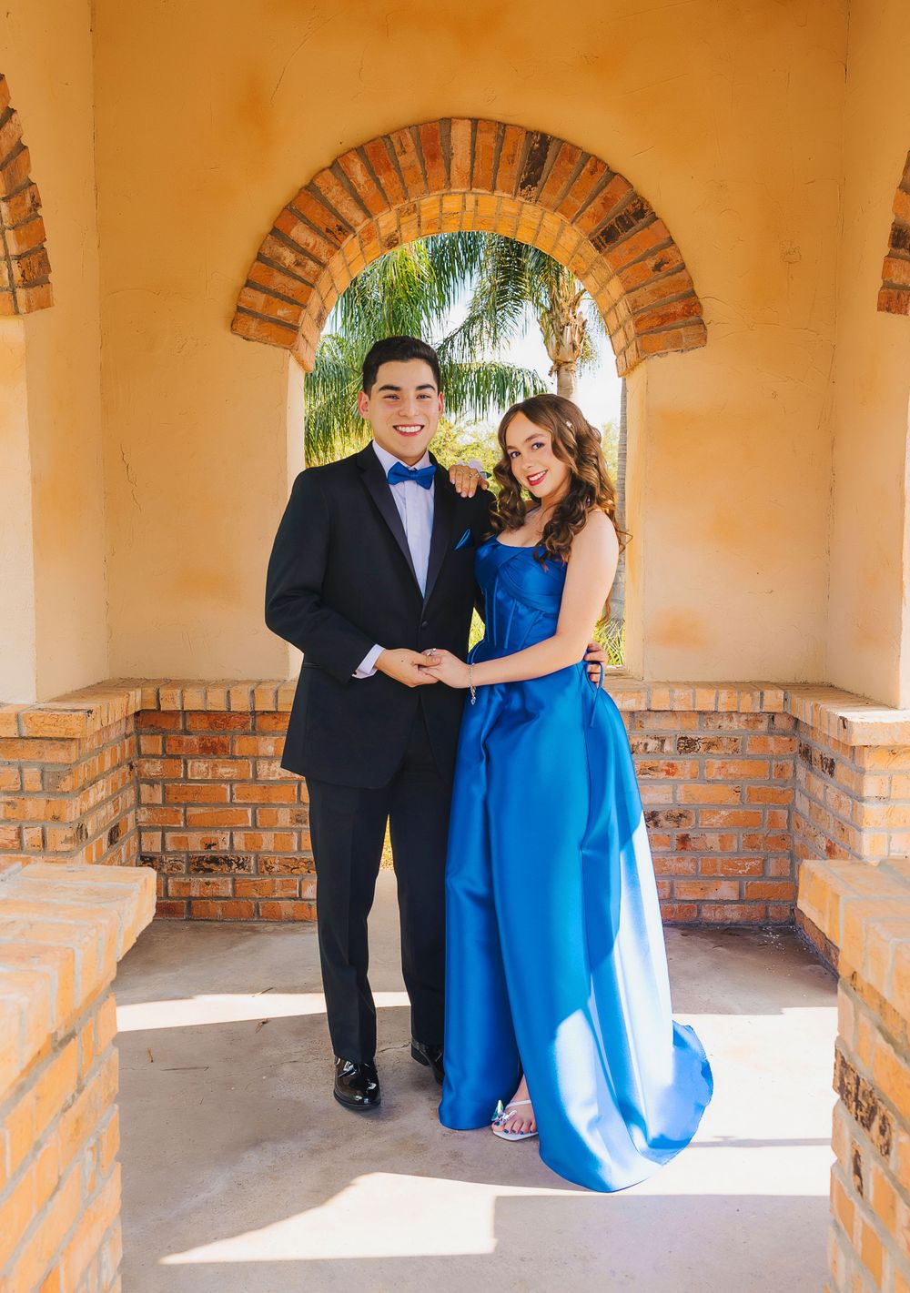 Formal portrait of couple under Mediterranean style archway in blue gown and tuxedo.