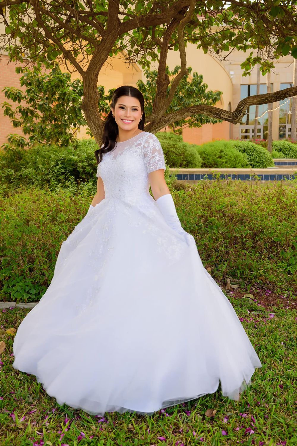 Outdoor bridal portrait featuring a flowing white ballgown with lace details near a brick building.