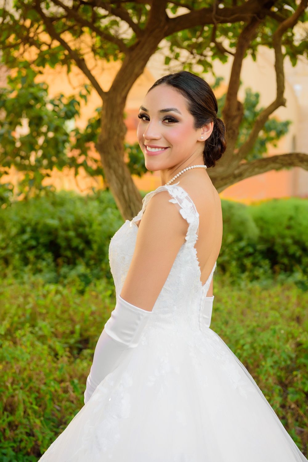 A bride in a white ball gown poses outdoors against a leafy background.