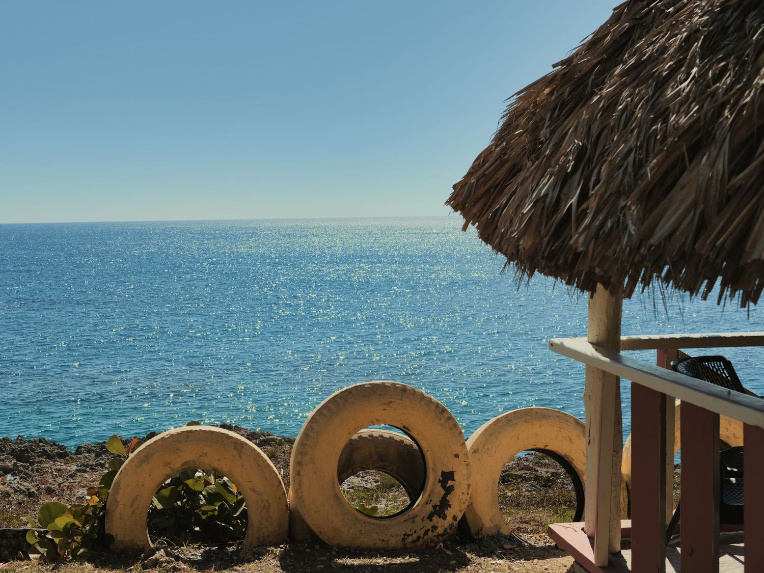 Tropical beach scene with circular stone sculptures and a thatched palapa overlooking blue ocean.
