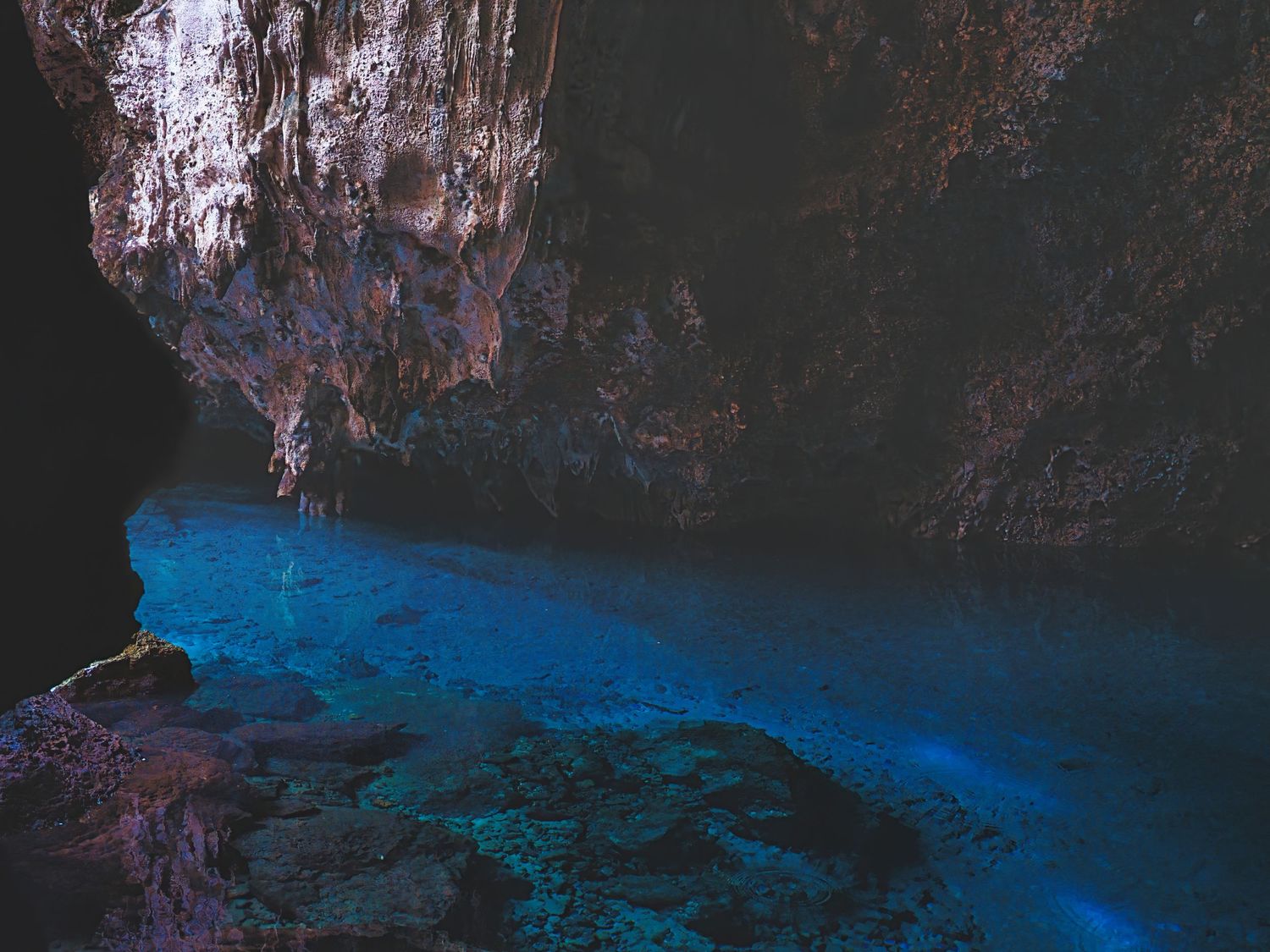 Stunning blue glowing underground cave pool with dramatic rocky ceiling and walls.
