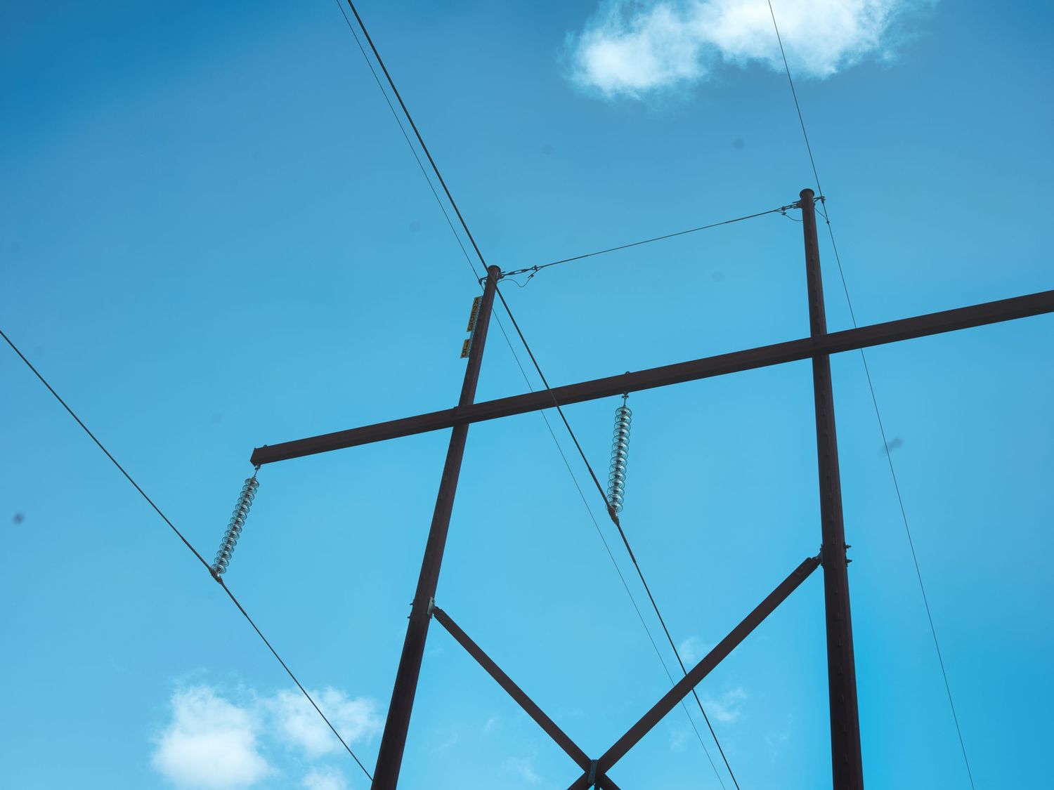 Low angle view of an electrical transmission tower against a bright blue sky with clouds.