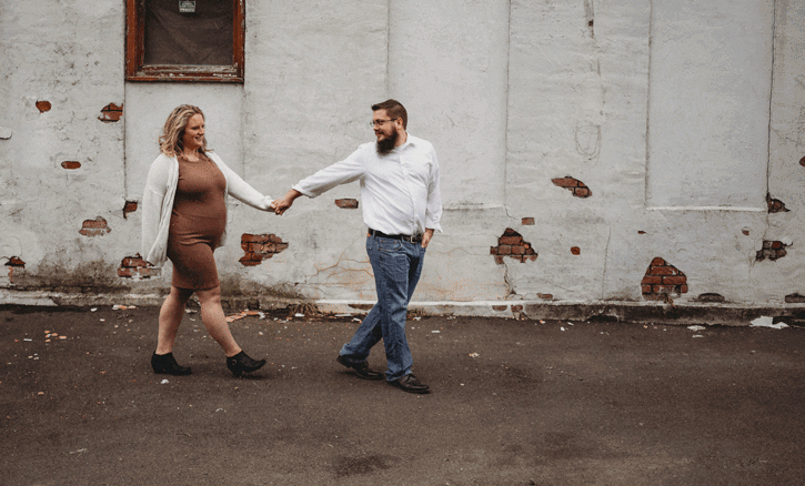 Couple holding hands and dancing together against an industrial concrete wall backdrop.