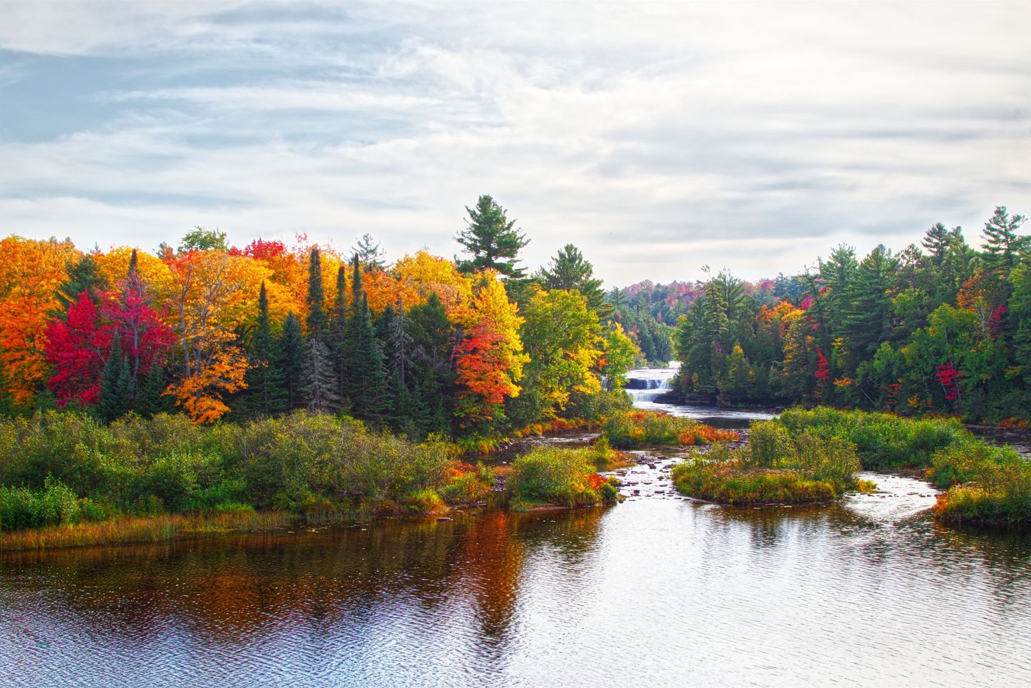 Tahquamenon Falls, Upper Peninsula, Michigan. Fall foliage surrounding waterfall, featuring red, orange, and yellow hues