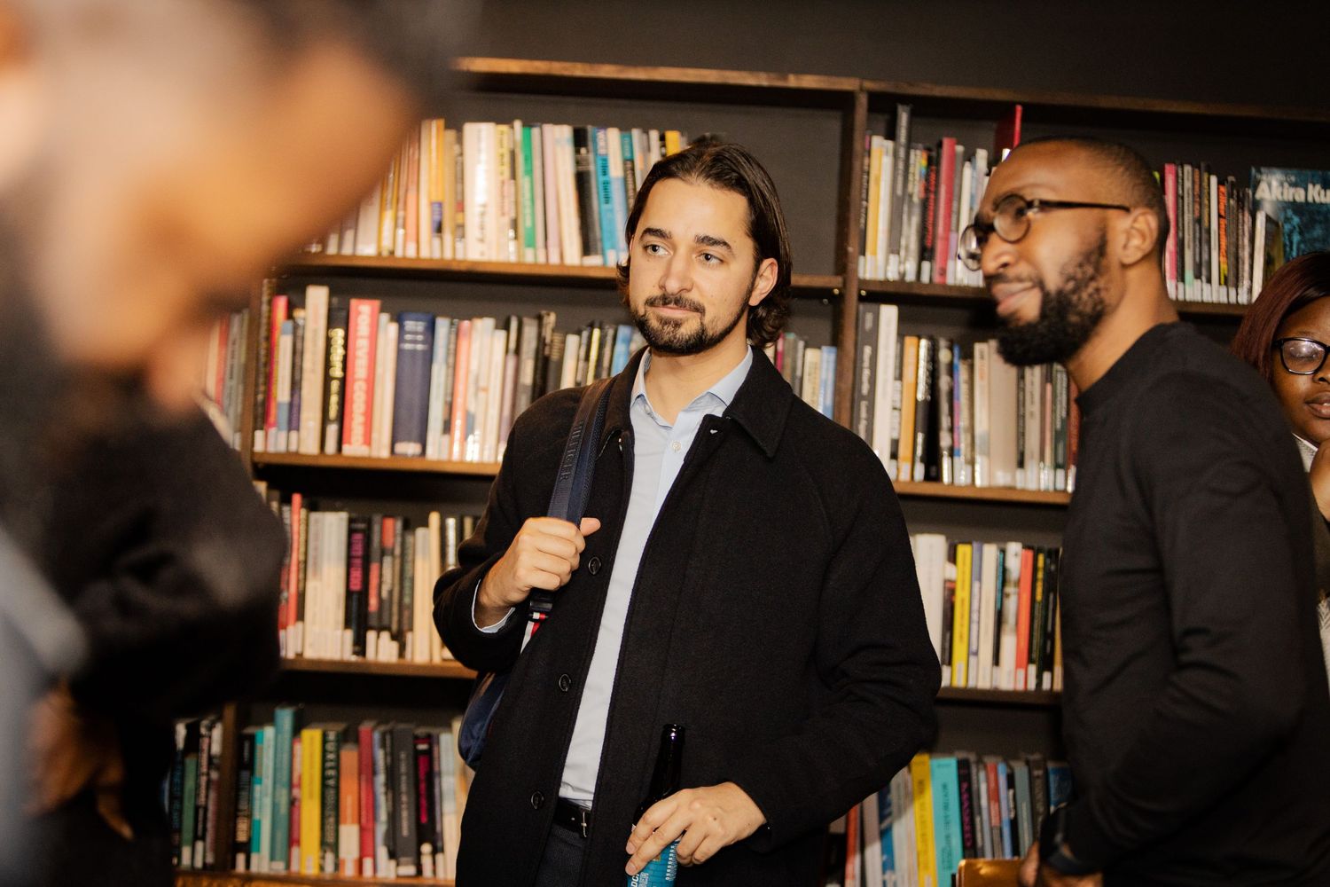 People engaged in conversation among bookshelves in a library or bookstore setting.