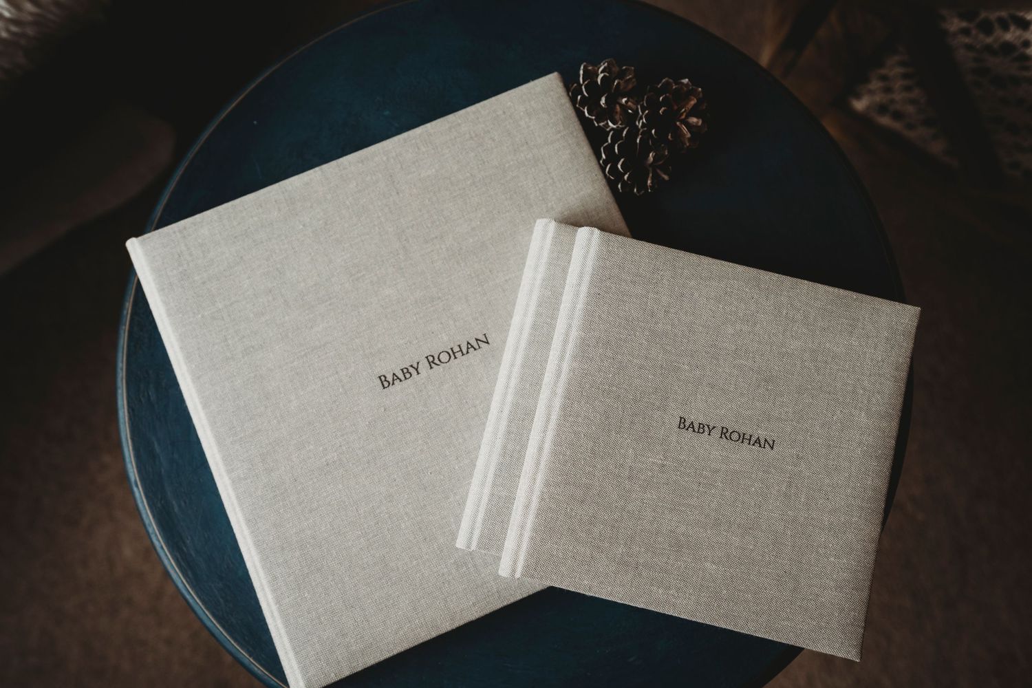 Two identical beige linen photo albums displayed on a dark blue surface.