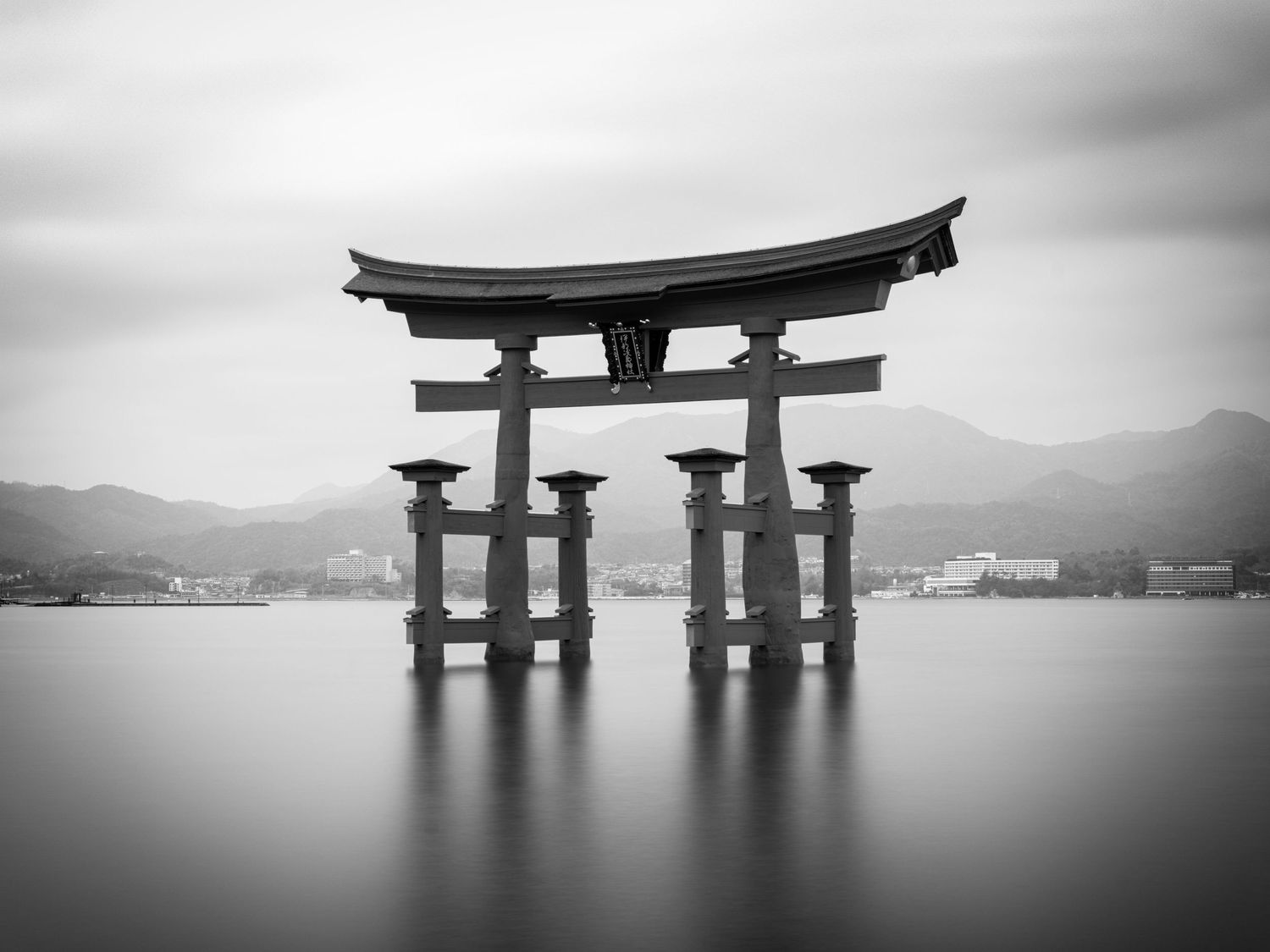 Minimalist black and white panorama of a traditional Japanese torii gate standing in calm water.
