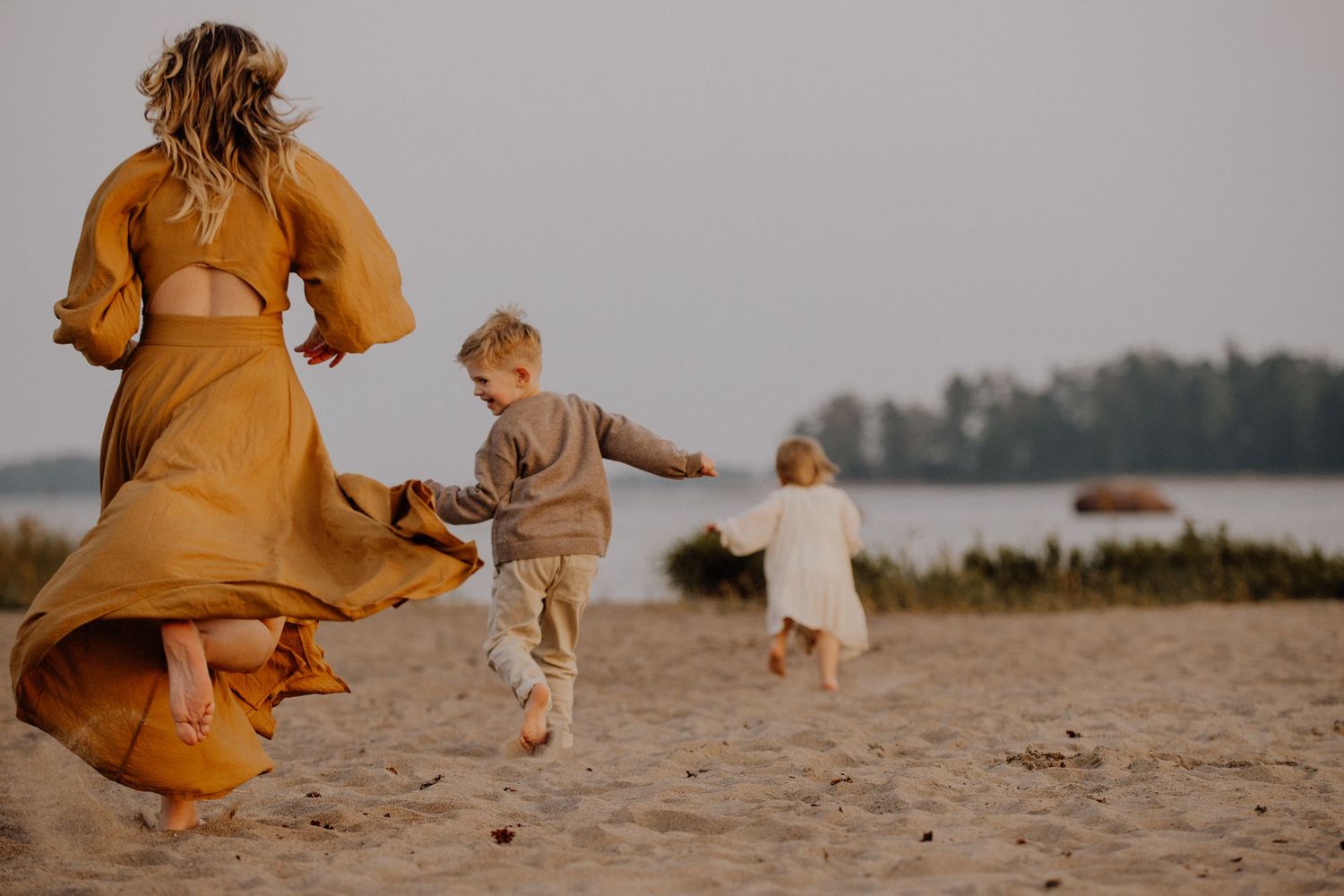 Family running and playing together on a sandy beach at sunset with flowing dresses creating a whimsical scene.