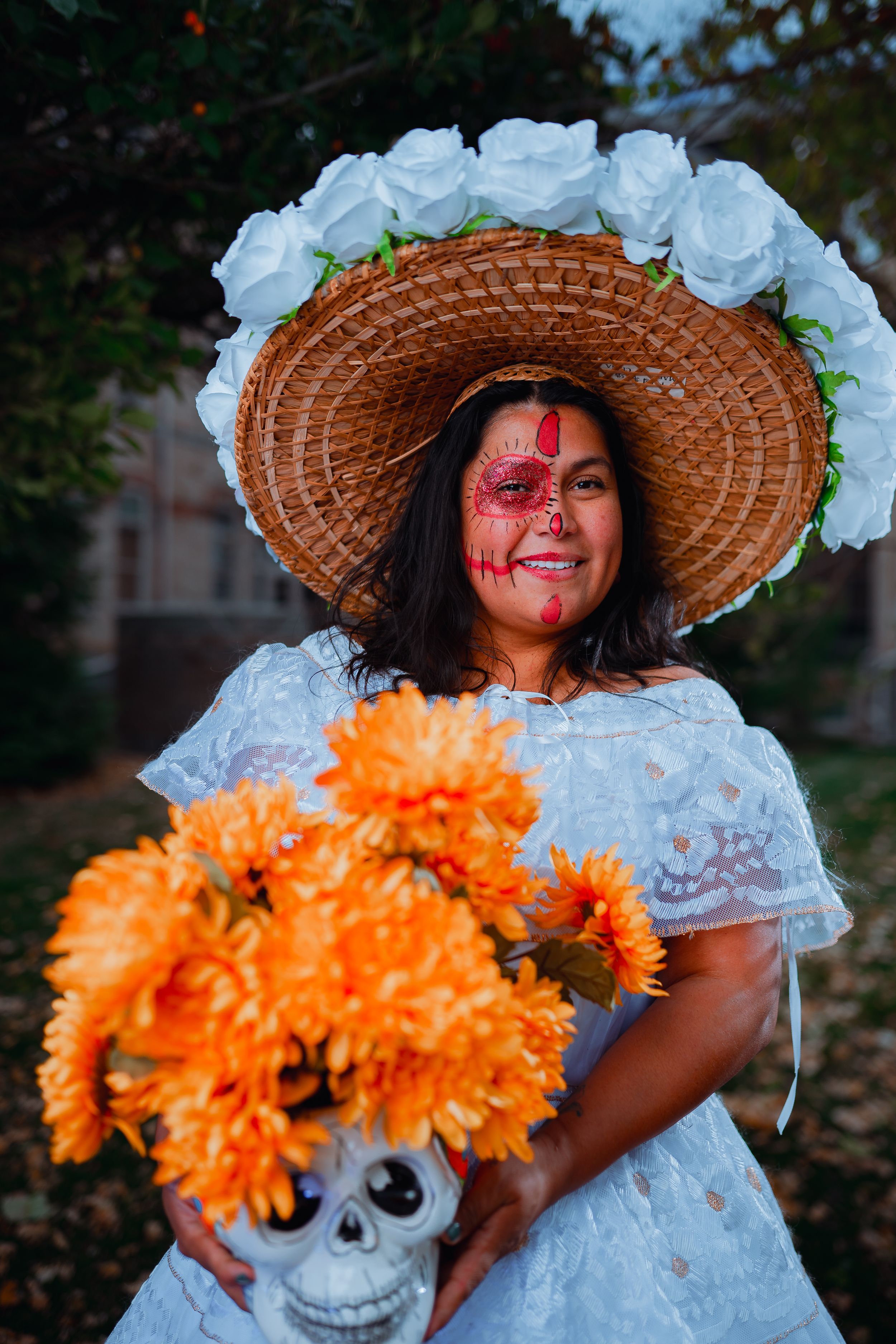 Traditional Dia de los Muertos portrait with decorated face, wide-brimmed hat, and orange marigold bouquet.