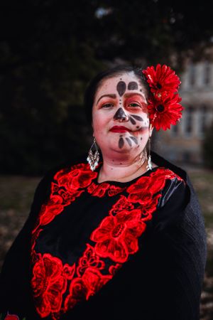 Person wearing traditional Dia de los Muertos face paint and red floral dress.