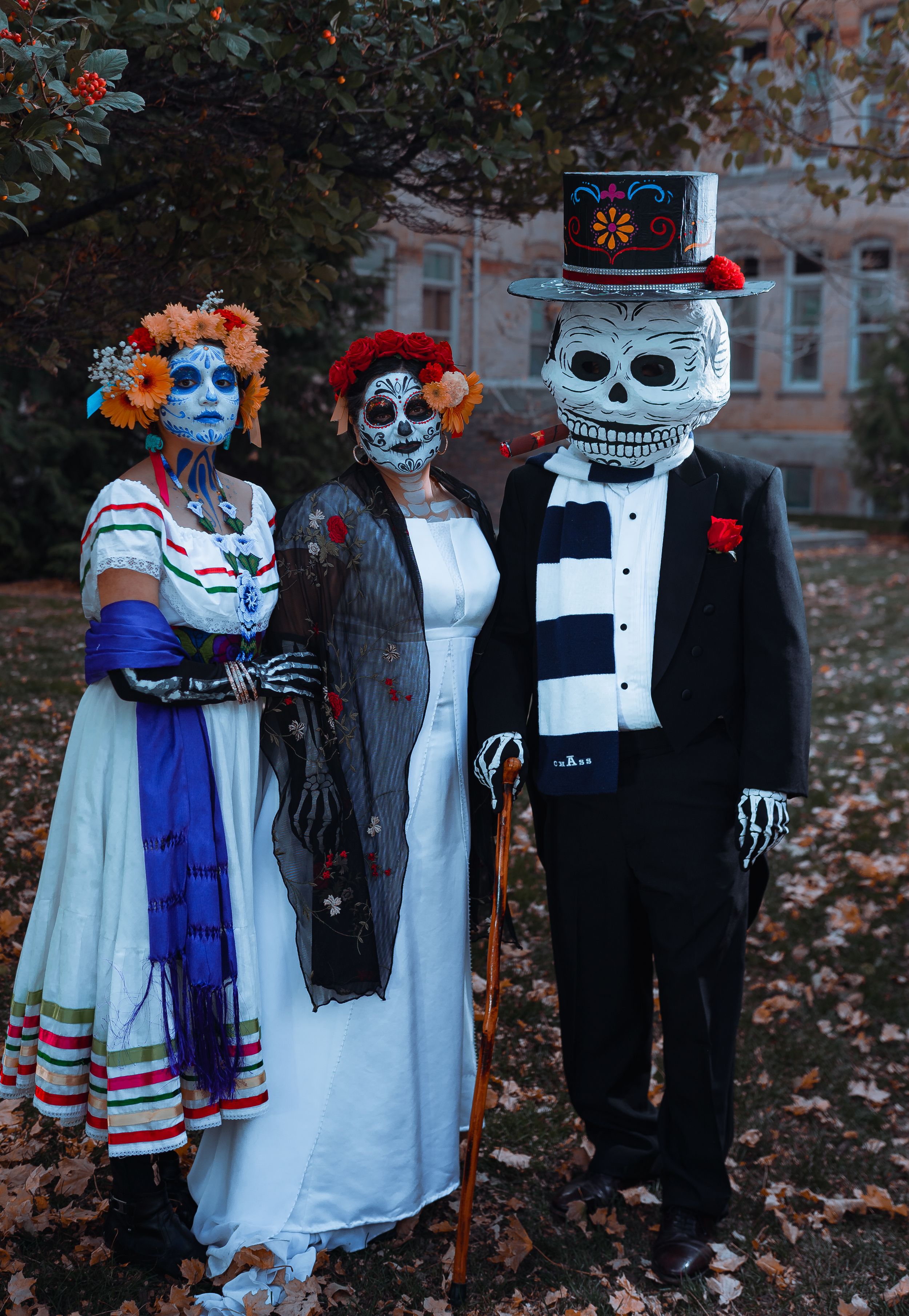 Three people in Day of the Dead skeleton makeup and costumes posing together outdoors.
